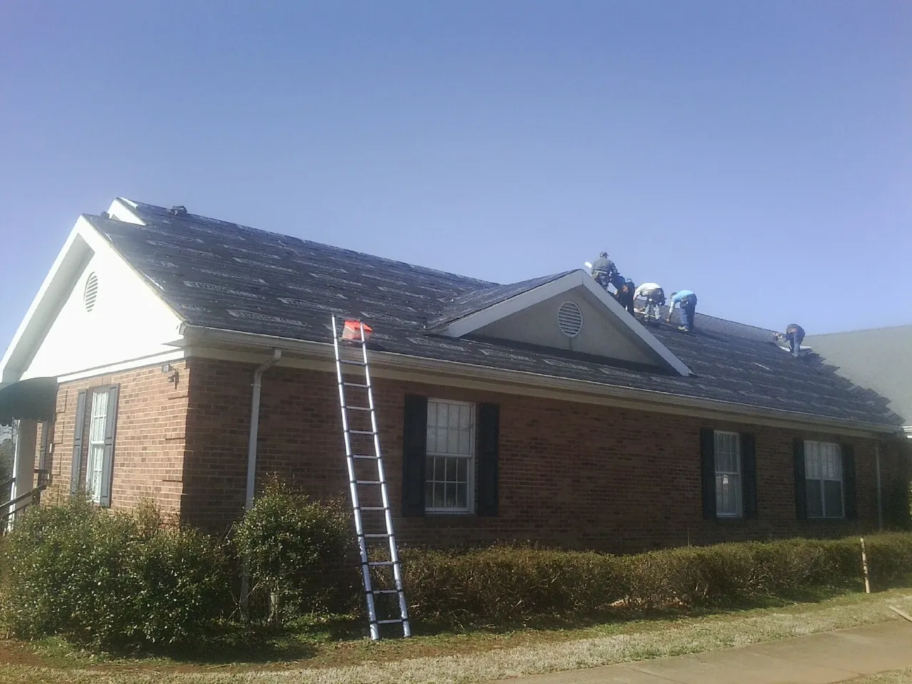 Crew tearing shingles off a brick ranch roof with a ladder set — Metal Roof Repair work by our crew in Southington