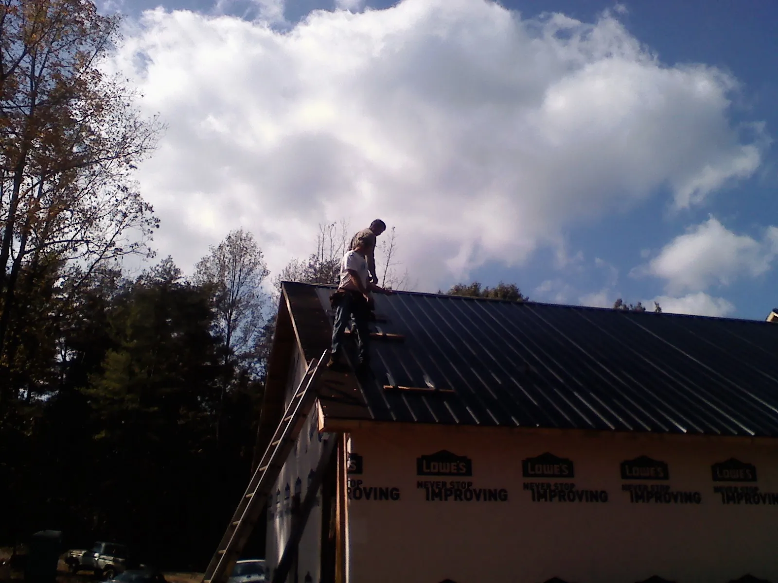 Roofer fastening dark metal panels high against a cloudy sky, from a Roof Inspection job in Southington