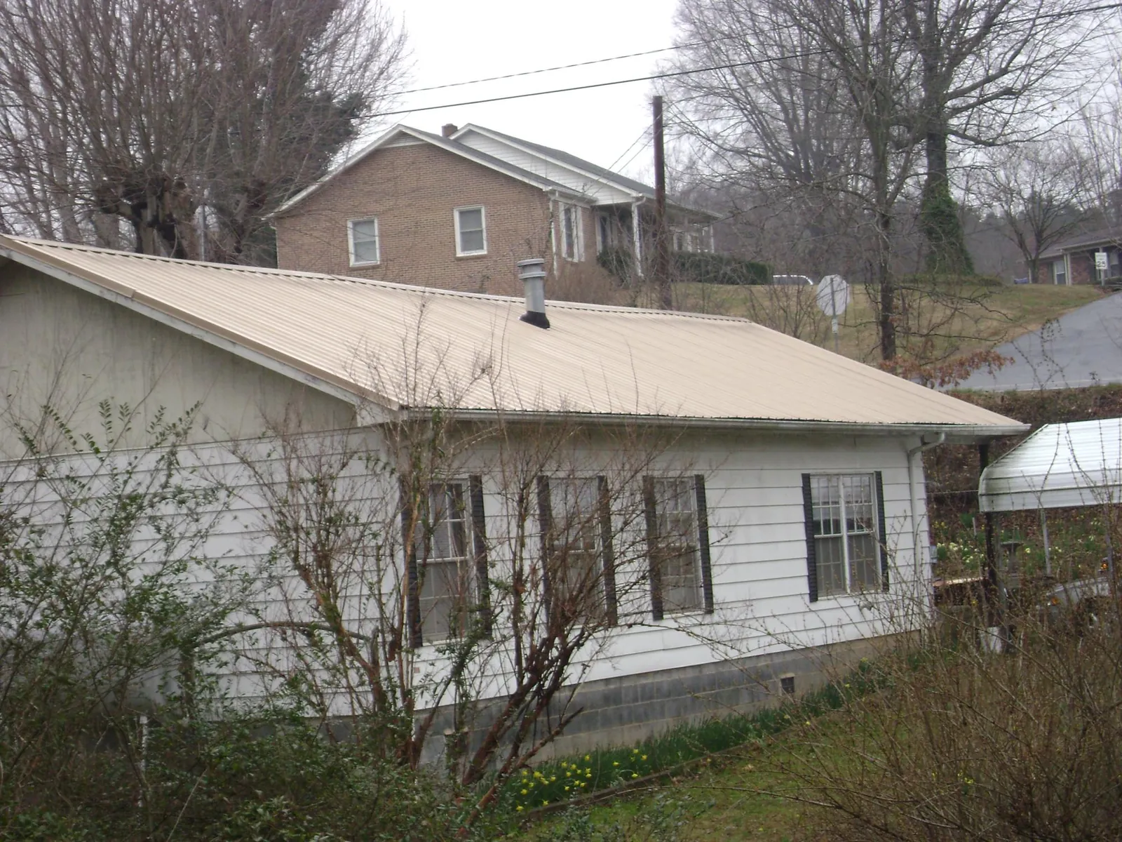 Tan metal roof on a white sided house set into a hillside — Commercial Roofing by Roofing Brothers in Southington